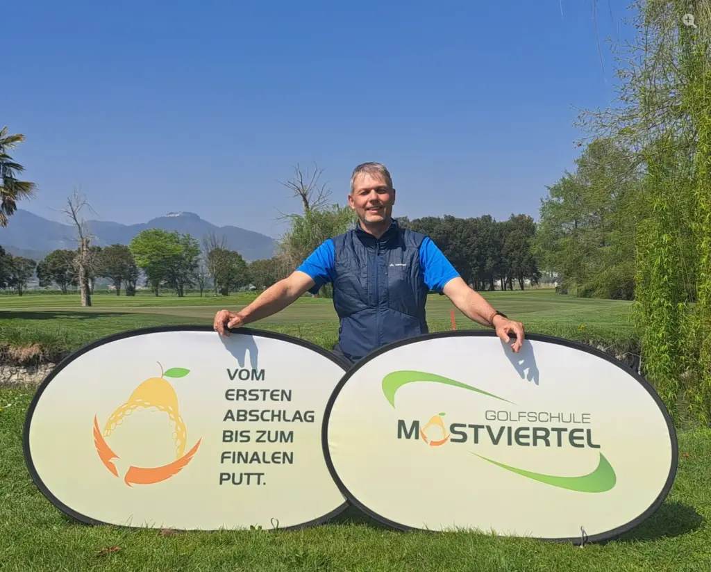 Golftrainer Manfred Krammer hinter zwei Werbeschildern der Golfschule Mostviertel