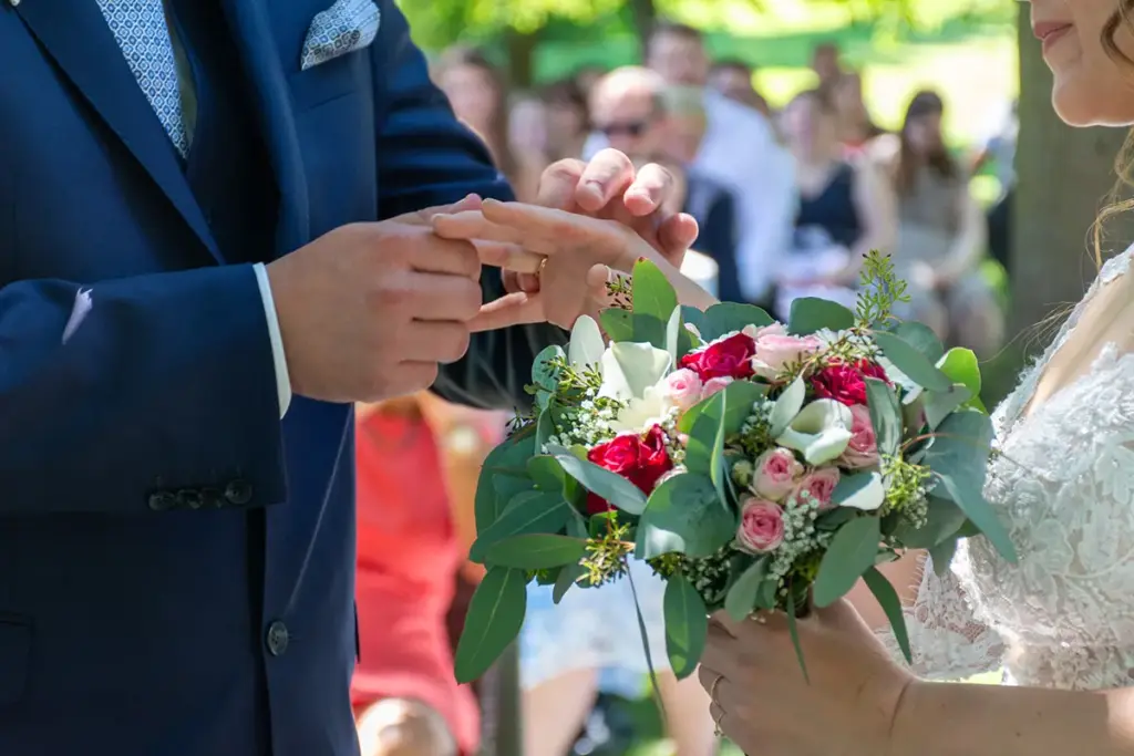Mann steckt Braut mit Brautstrauss den Ring an bei einer Hochzeit am Golfplatz